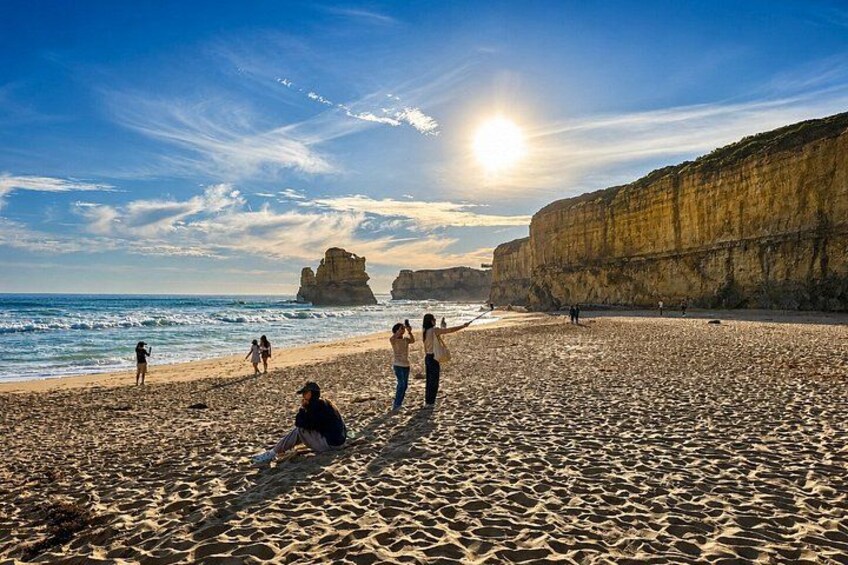 A beach with people walking and sitting, cliffs in the background, and the sun setting. 1