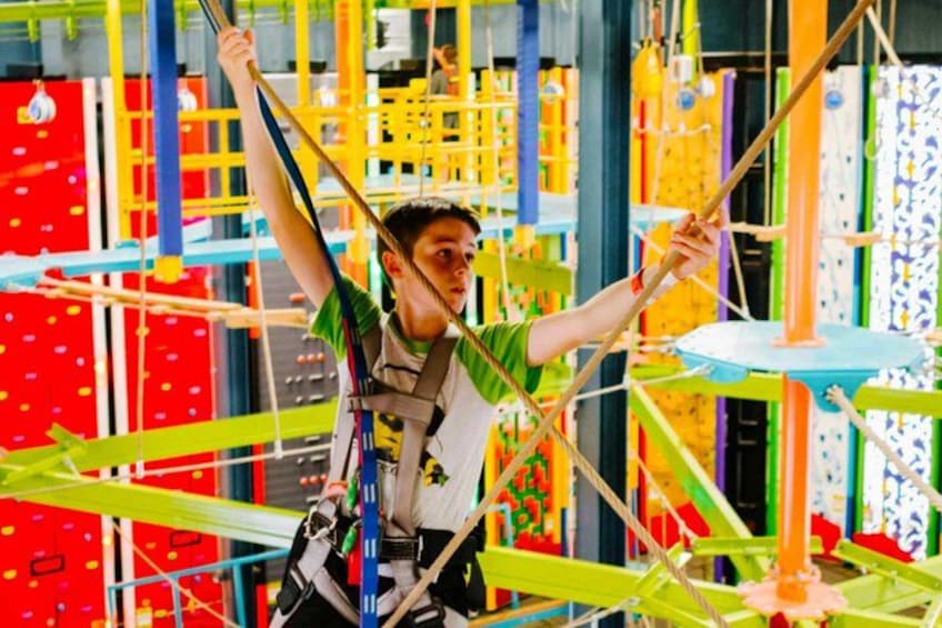 A person navigating a colorful obstacle course with ropes and nets. 2
