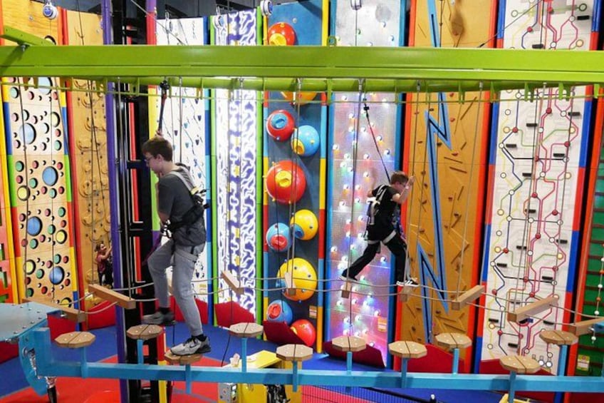 Two people navigating a rope course with colorful obstacles and a netted floor. 4