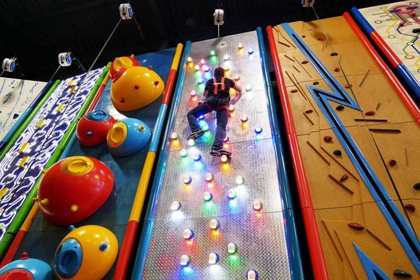 A person climbing a brightly lit climbing wall with colorful holds. 2