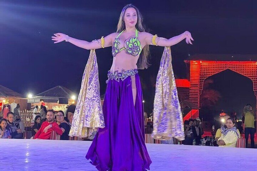 A belly dancer performing on a stage with an audience in the background. 4