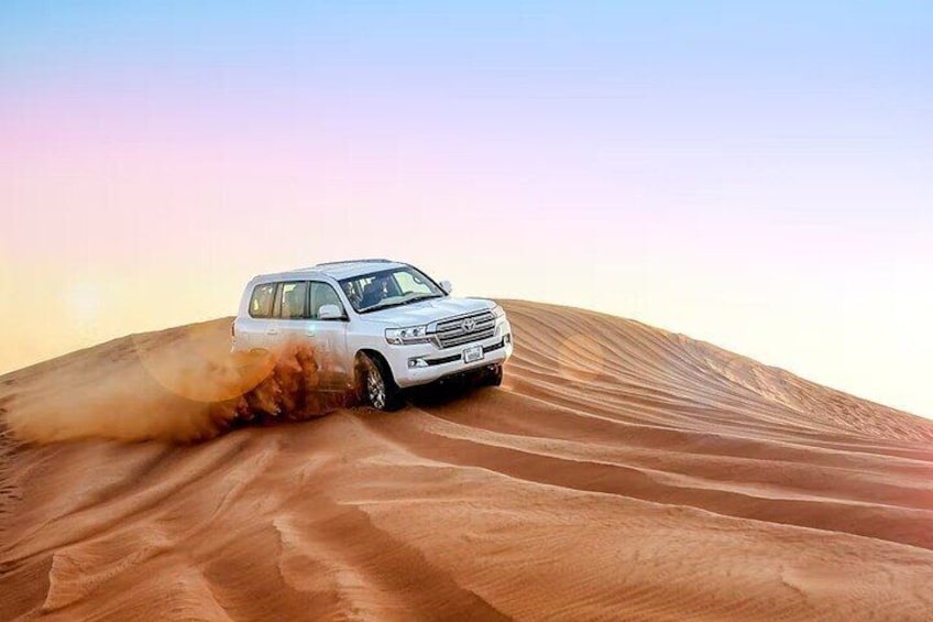 A white SUV driving through a desert with sand dunes. 1