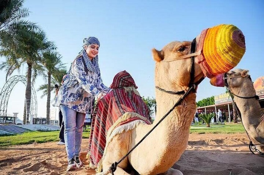 A camel with a colorful blanket, a person leading it, and palm trees in the background. 4