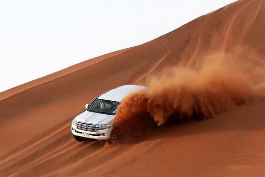 A white vehicle driving through a sandy desert landscape. 5