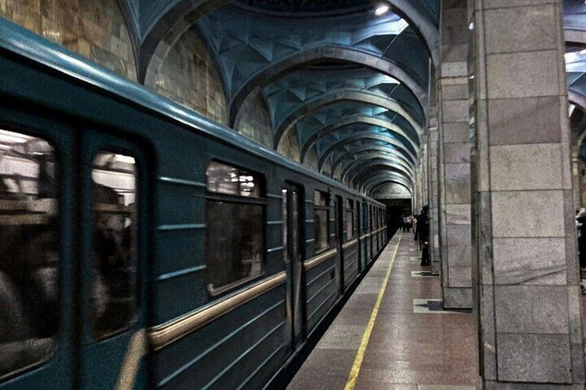 A subway train in a station with arched ceilings and stone pillars. 4