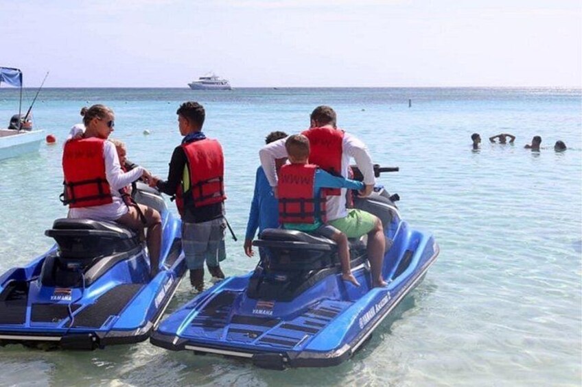 People on jet skis in shallow water with a boat in the background. 5
