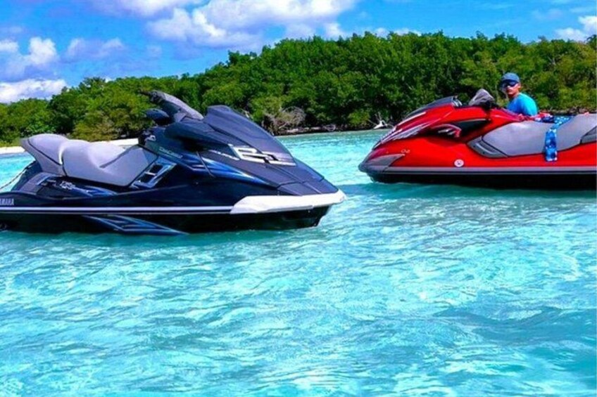 Two jet skis on clear turquoise water with a forested island in the background. 1