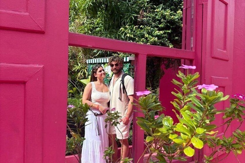 A couple standing in a garden with a pink gate and lush greenery. 2