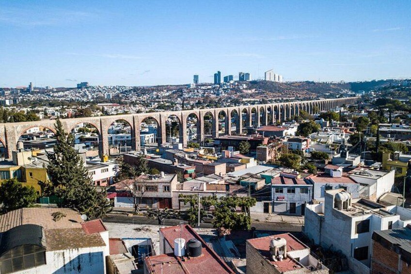 A cityscape with a prominent aqueduct spanning across the foreground, a dense urban area with various buildings, and a distant city skyline with high-rise buildings. 3