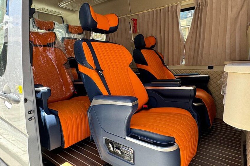 A campervan interior with orange and black seats, a small table, and a window with curtains. 3