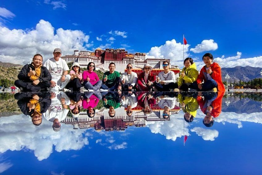 A group of people sitting on a reflective surface with a traditional building and mountains in the background. 1