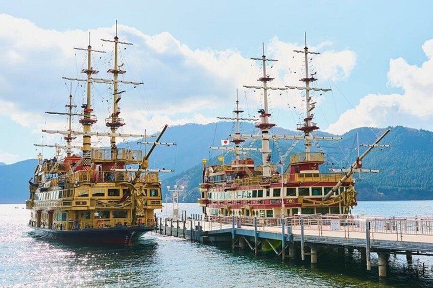 Two large, ornate ships docked at a pier with mountains in the background. 2