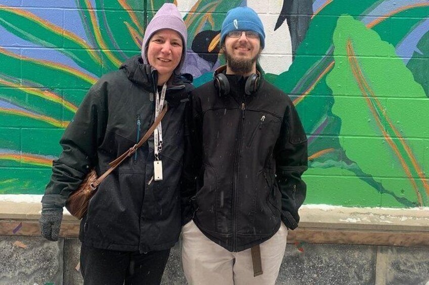 Two people standing in front of a colorful mural with abstract designs. 5
