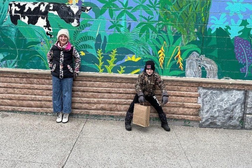 Two people sitting on a bench with a mural in the background. 2
