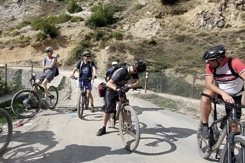 A group of cyclists on a paved path with a dirt hill in the background. 1