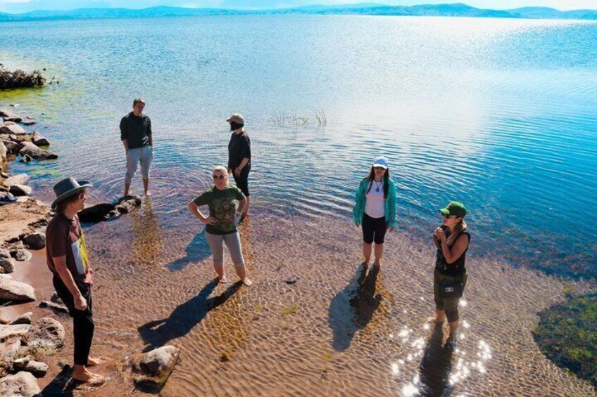 En gruppe mennesker står på en klippefyldt strand ved en stille sø. 2