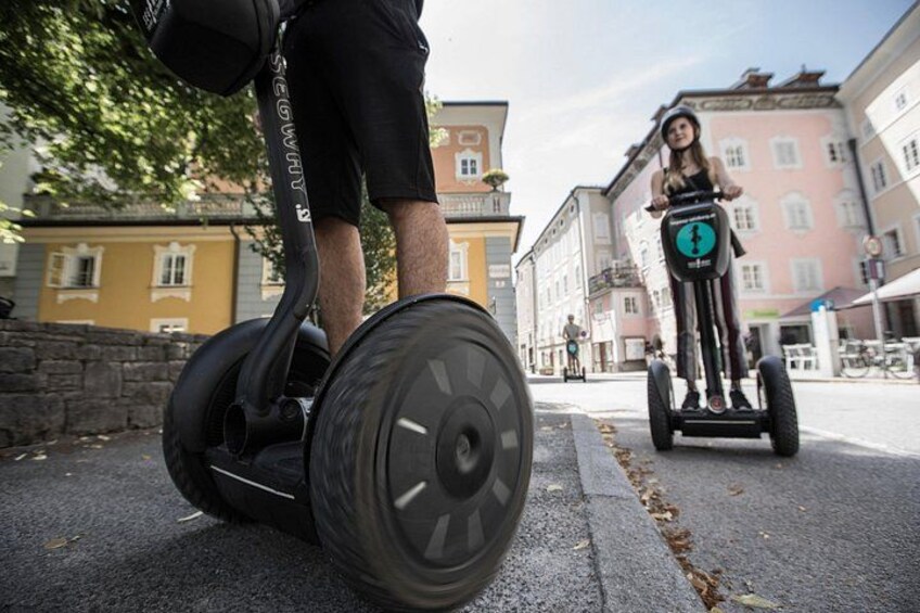 Two people riding Segway scooters on a street with buildings in the background. 4