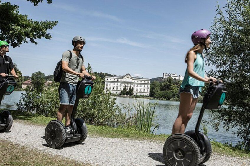 Three people on Segways near a body of water with buildings in the background. 3