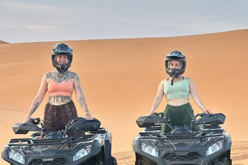 Two people on quad bikes in a desert with sand dunes in the background. 3