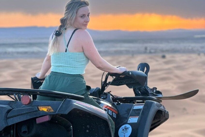 A person riding a quad bike on a sandy terrain with a sunset in the background. 4