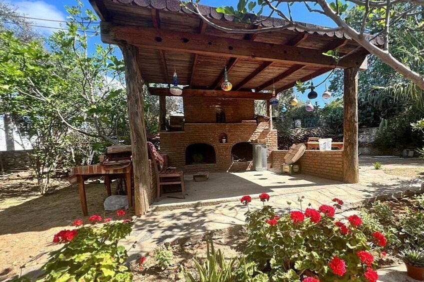 A rustic outdoor kitchen with a brick oven, wooden furniture, and a garden with red flowers. 3
