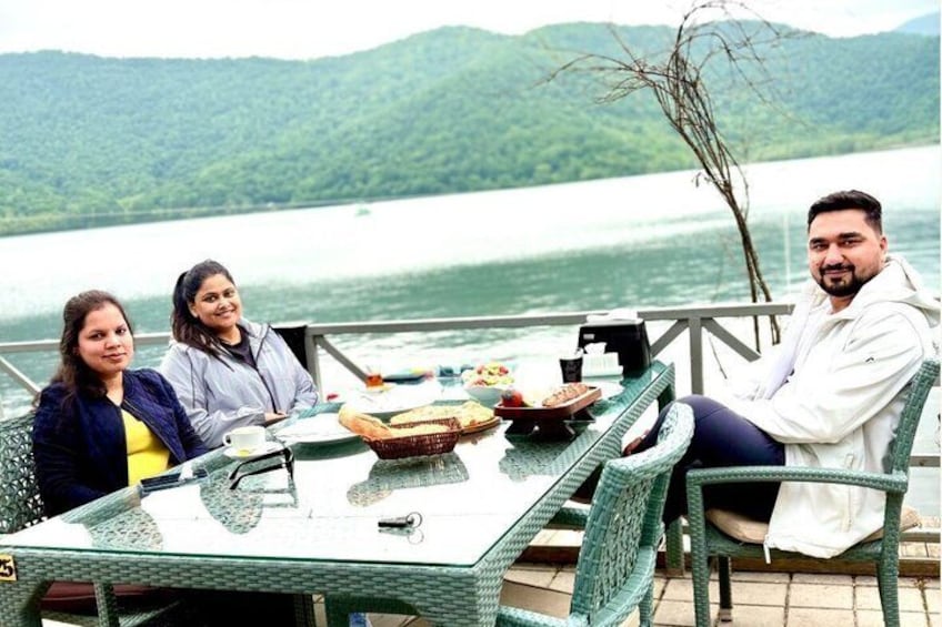 A group of people dining at a table by a lake with mountains in the background. 3