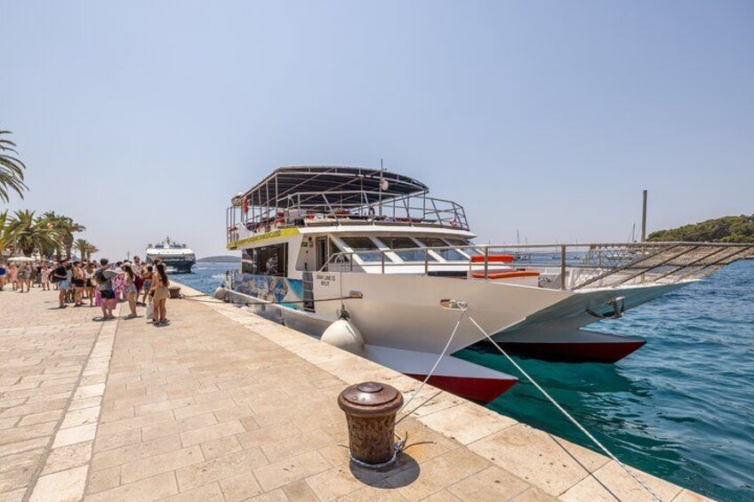 A boat docked at a pier with people on the shore and another ship in the background. 2