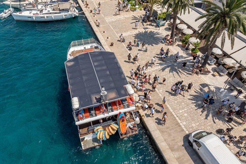 A ferry docked at a pier with people walking around and a palm tree in the background. 4