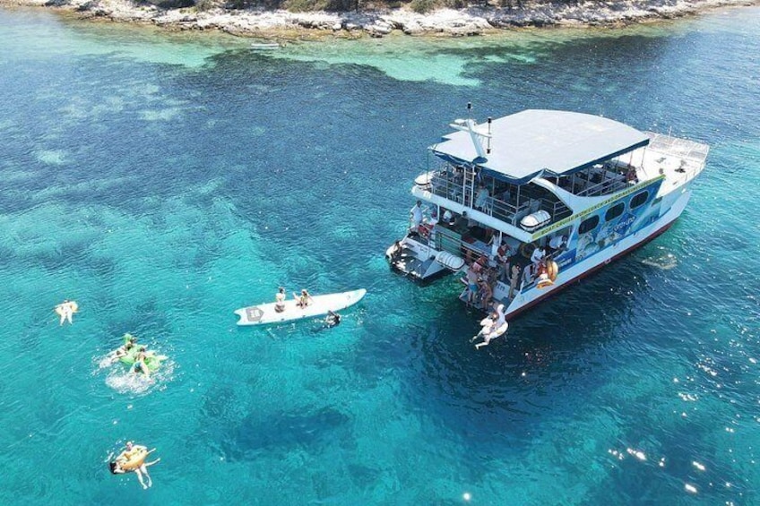 A large boat with passengers and a smaller boat nearby in clear blue waters. 5