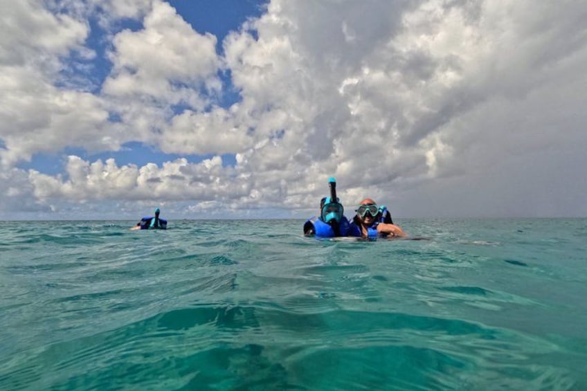 To personer snorkler i turkis vand under en delvis skyet himmel. 3