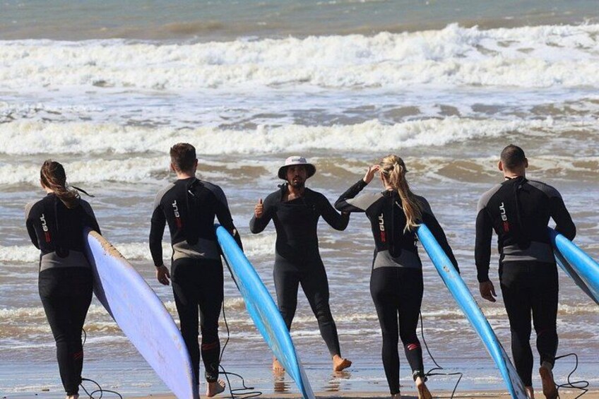 Eine Gruppe von Personen in Neoprenanzügen trägt Surfbretter an einem Strand. 4
