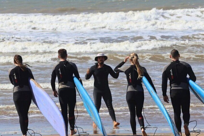 Un grupo de personas con trajes de neopreno cargando tablas de surf en una playa. 4