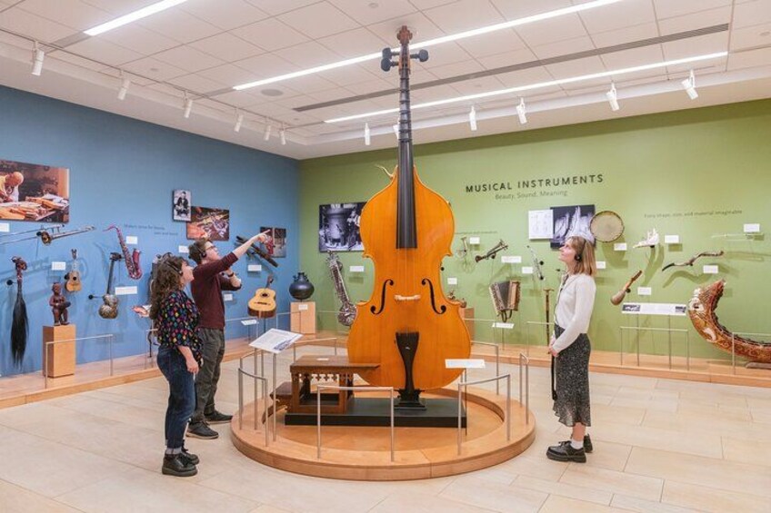 Una exposición de museo con instrumentos musicales, incluyendo un gran violonchelo, exhibidos sobre pedestales. 1