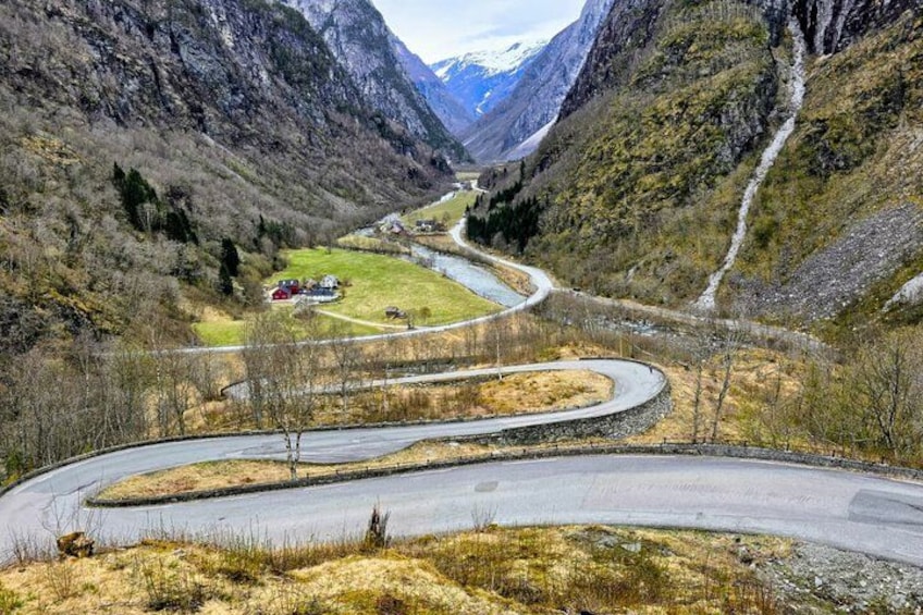 A winding road through a mountainous valley with a small settlement and a river. 3