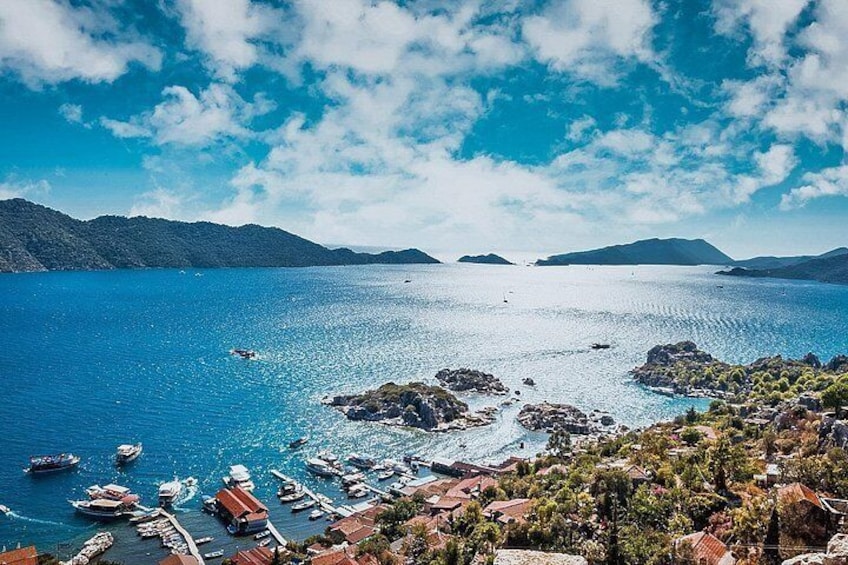 A coastal town with boats docked, a clear blue sea, and distant mountains. 4