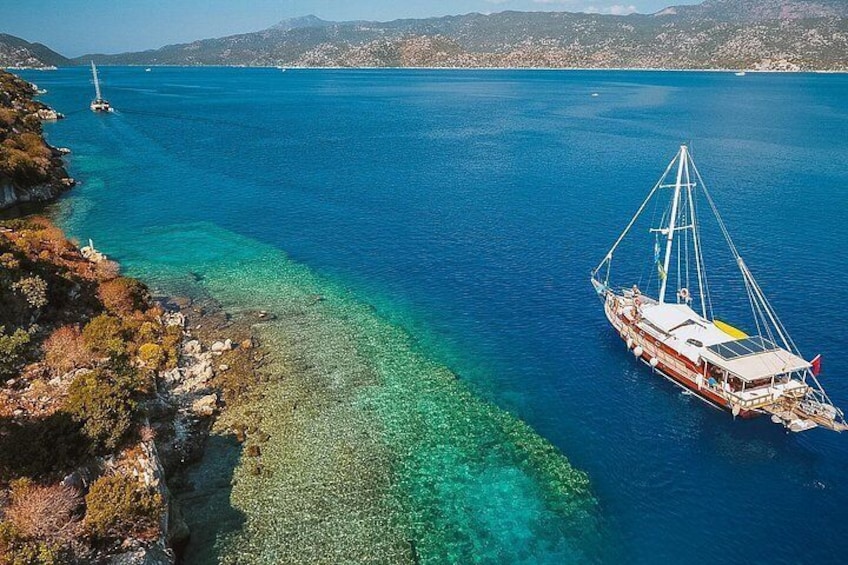 A boat on a clear blue sea with a rocky shoreline and distant mountains. 3
