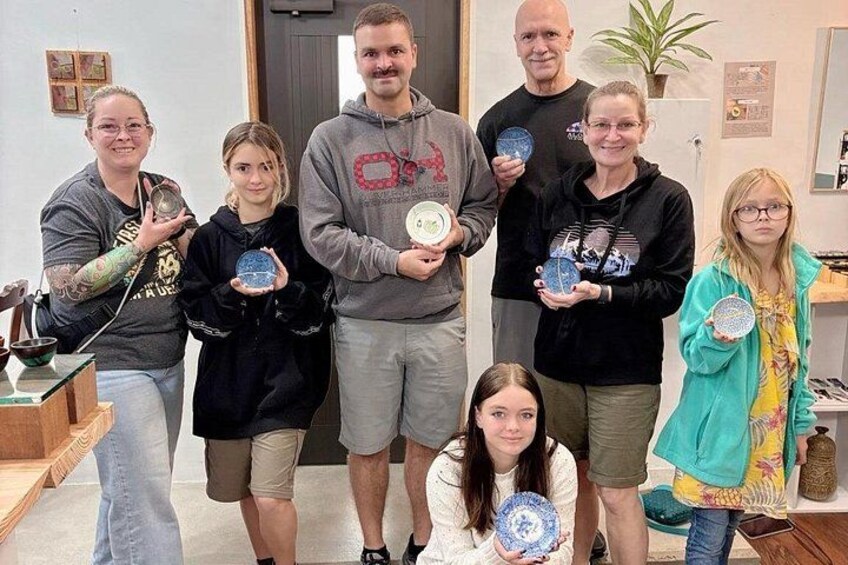 A group of people holding plates with blue and white designs, standing indoors with a plant and a door in the background. 3