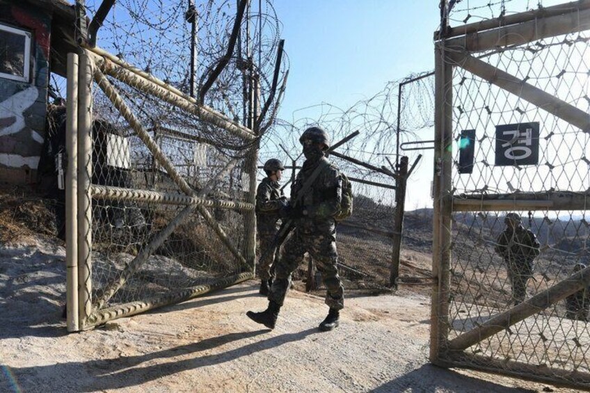 A metal gate with barbed wire, a soldier in camouflage, and a sign with Korean characters. 4
