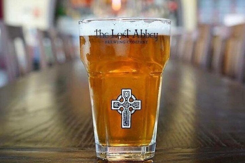 Et glas øl med et kors logo og teksten 'The Lost Abbey Brewing Company' på et træbord. 3