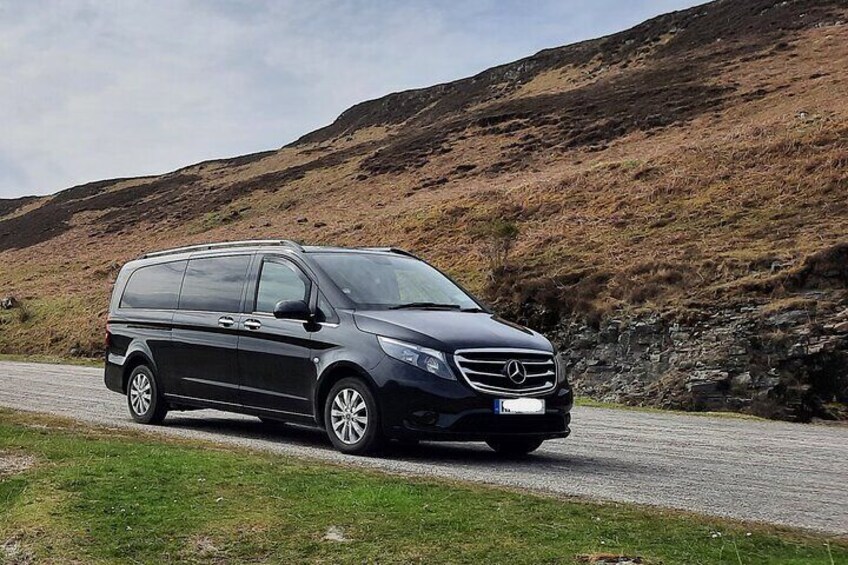 Un fourgon Mercedes-Benz Sprinter noir est garé sur une route, avec un paysage montagneux en arrière-plan. 2