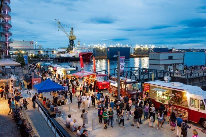 A busy waterfront with food trucks, a dock, and a crowd of people. 2