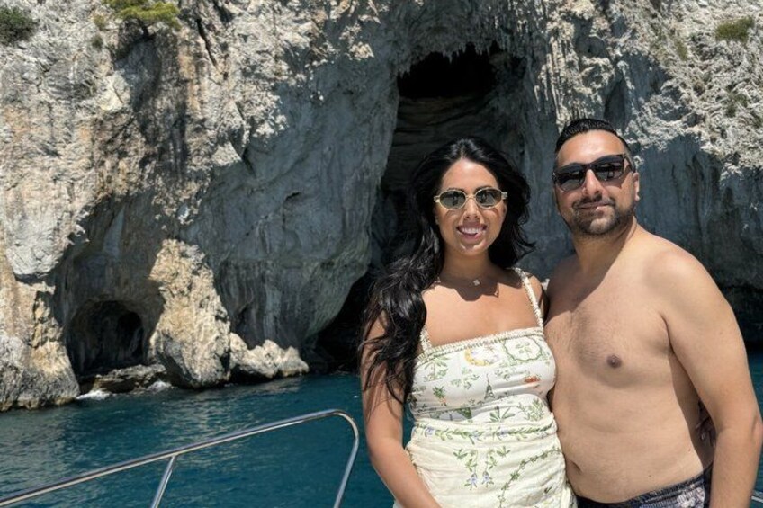 Une côte rocheuse avec l’entrée d’une grotte, un bateau et deux personnes debout au bord de l’eau. 3