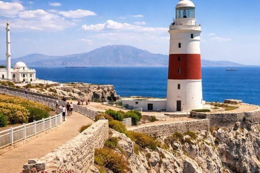 A lighthouse, a stone wall, and a clear blue sea with mountains in the background. 5