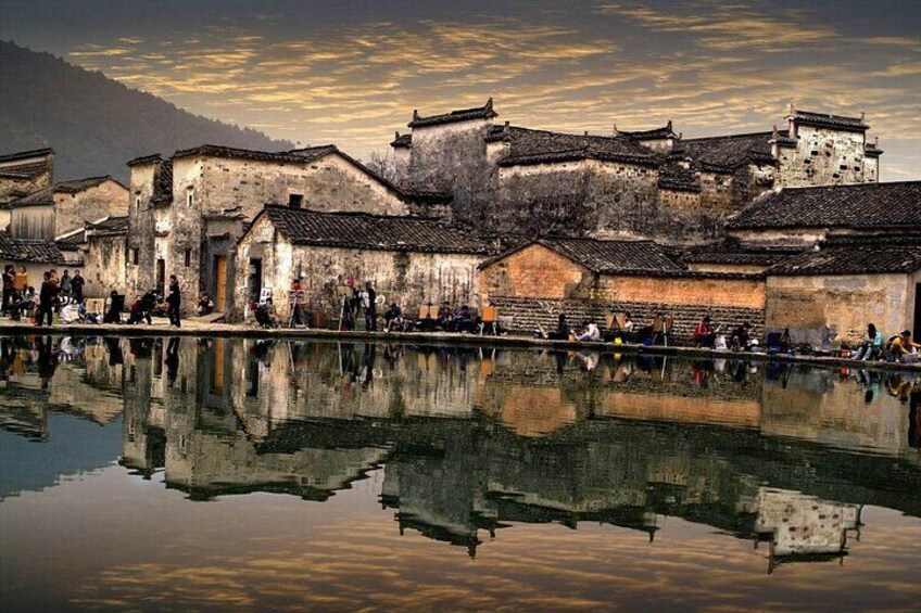 Traditional buildings, a calm water body reflecting the structures, and a mountainous backdrop. 4