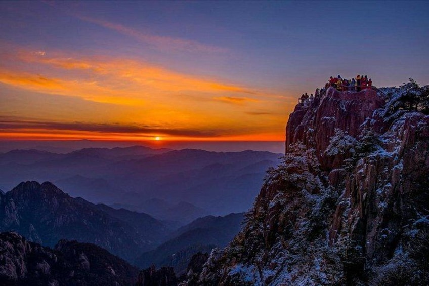 A sunset over a mountainous landscape with a group of people on a cliff. 1