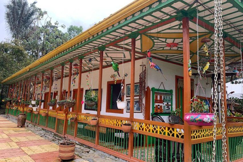 A colorful outdoor structure with a covered seating area, decorative hanging elements, and potted plants. 2