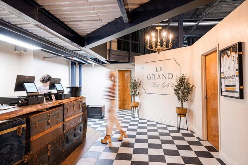 A checkered floor, a wooden desk, a chandelier, and a sign that reads 'LE GRAND Mini Golf'. 1