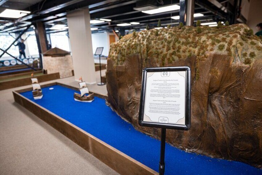A large rock with a blue base, two model ships, and an informational sign. 3