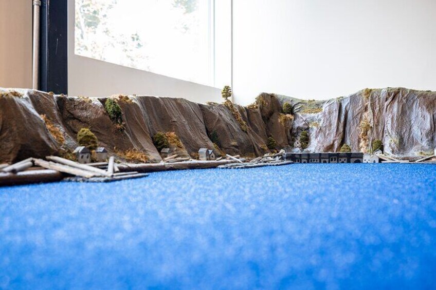 A model landscape with a blue carpet, model trees, and a small house. 4