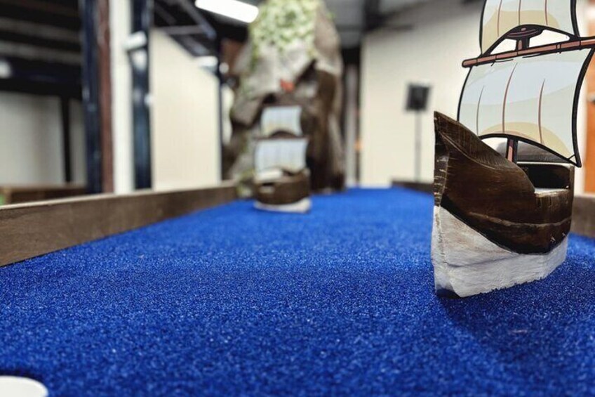 A model ship on a blue carpet, a wooden ship model, and a person in the background. 1